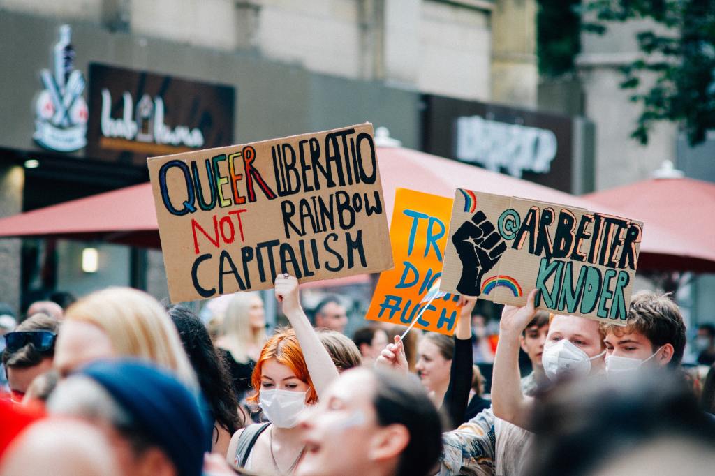 A protest for LGBTQ+ rights. A woman holds a placard with the message: Queer liberation, not rainbow capitalism